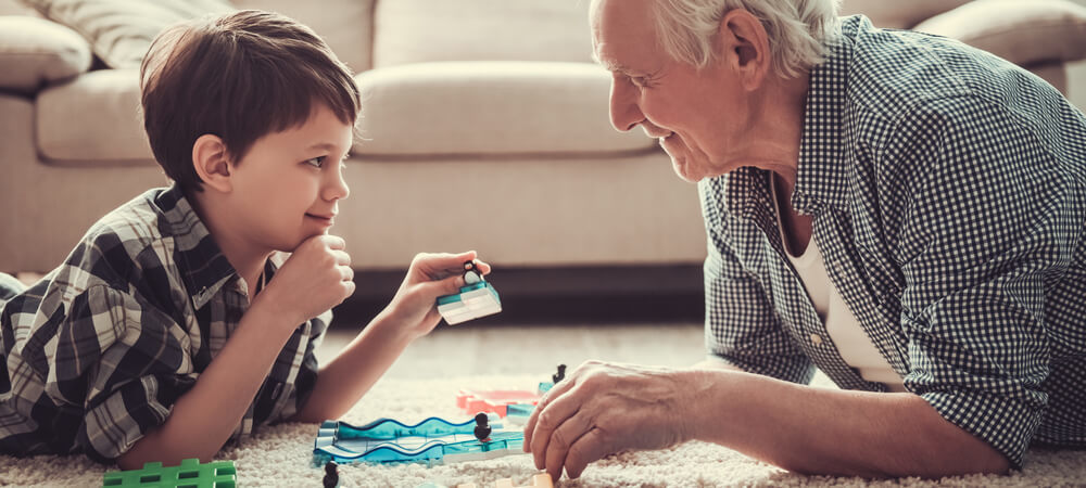 A grandson is playing a game on the floor with his grandfather.