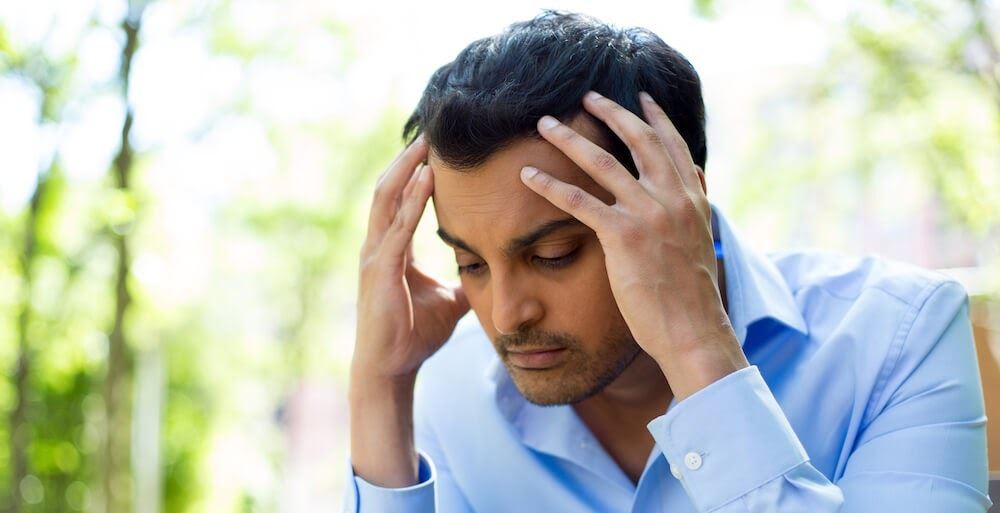 A man is sitting down while grabbing his head.