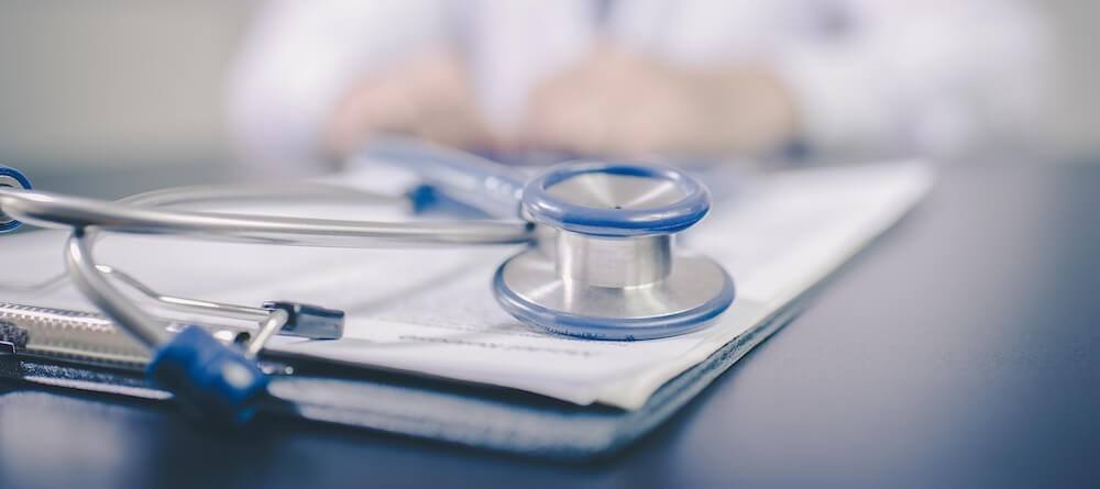 A stethoscope is on a doctor's desk with some medical records. 