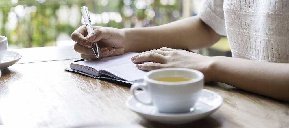 A woman is sitting at a table with a journal and a cup of tea.