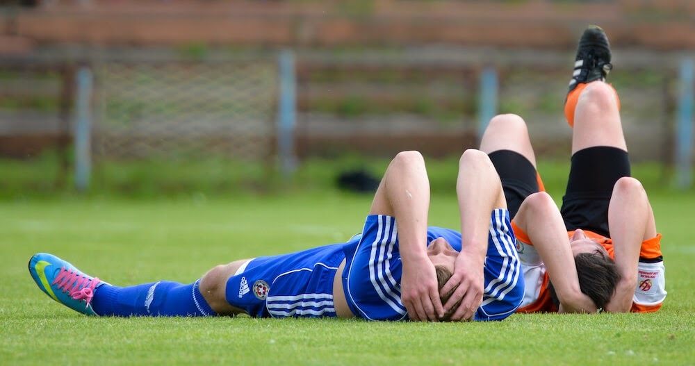 Two soccer players are lying on the field after a rough game.