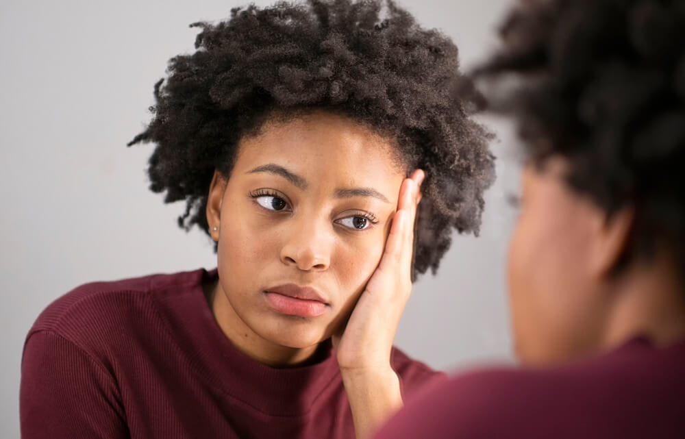 A woman is holding her cheek while looking in the mirror.