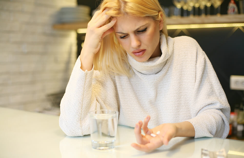 Woman sitting at table taking medication for head pain