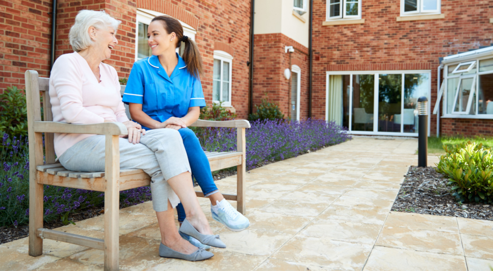 Elderly woman sits with nurse in a park. 