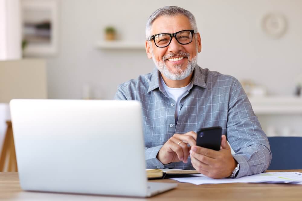 Man wearing glasses using mobile phone and laptop