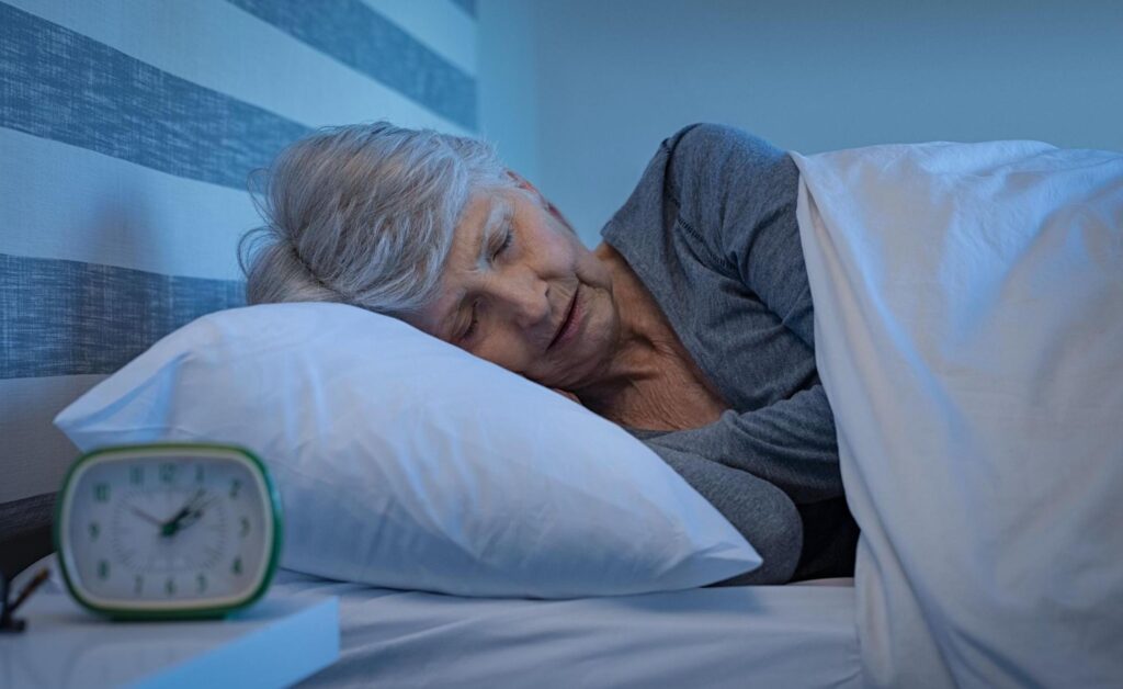 Senior woman sleeping in bed with alarm clock on the nightstand
