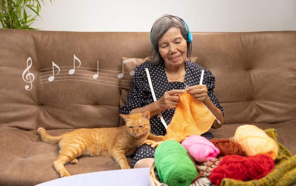 Senior woman knitting on the couch while listening to music